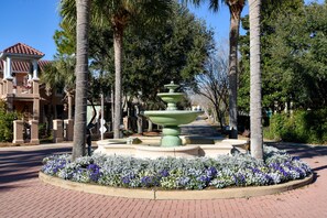 Stunning central fountain surrounded by a vibrant flower bed and palm trees, set amidst a serene landscaped area.