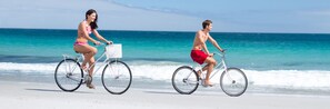 Dos personas andan en bicicleta por la playa, con el océano al fondo.