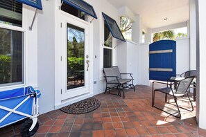 A covered patio area with a white door, two chairs, a table, and a blue stroller. - Private Home with Carriage House in Exclusive Gated Caribe Community (Miramar Beach)
