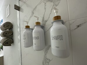 Three white bottles with labels on a marble-tiled wall, one labeled "BODY WASH" and another "SHAMPOO". - Green Luxurious 5BD Jungle House by FL Keys MIA (Florida City)
