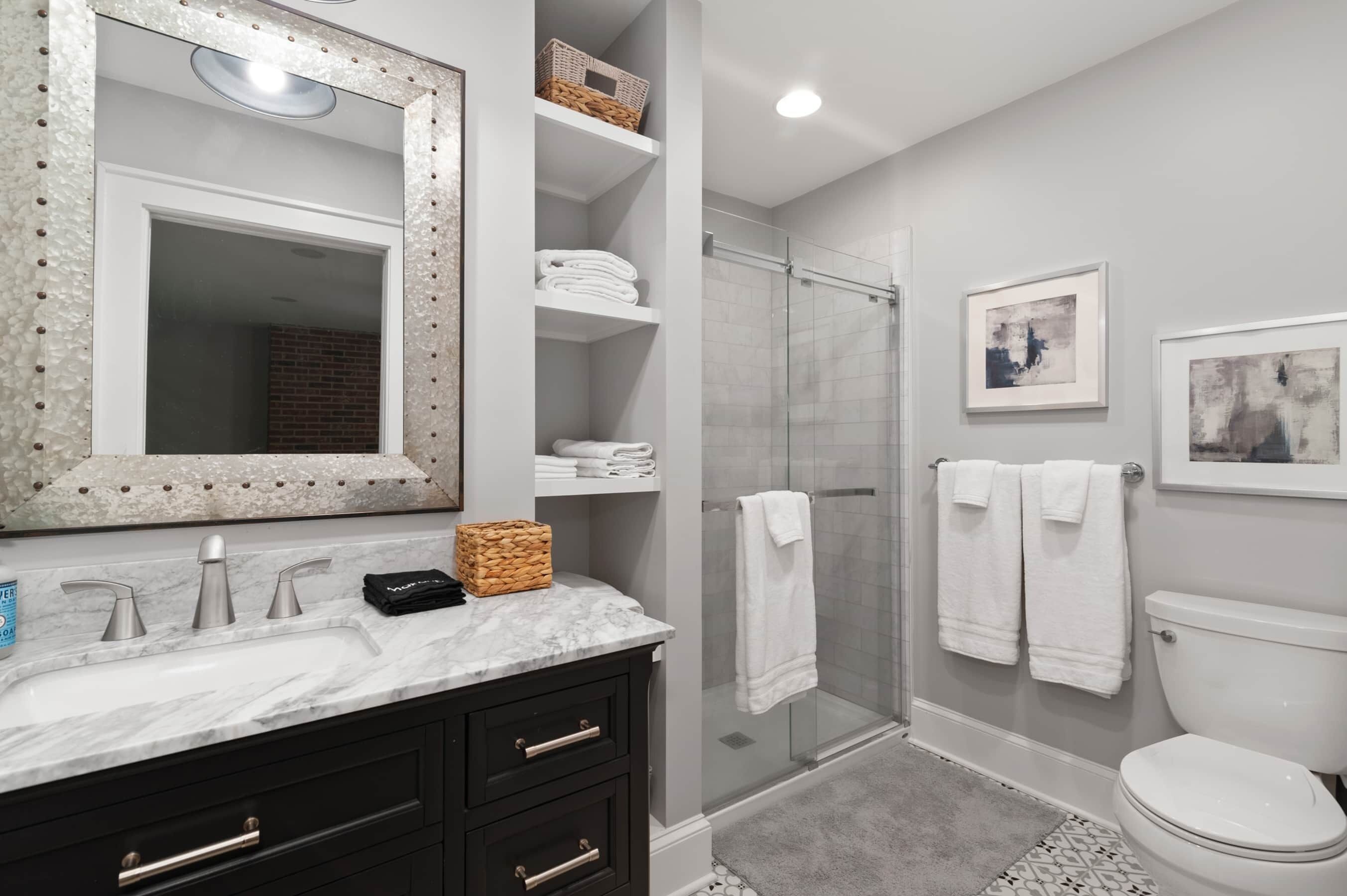 Un baño moderno con lavamanos de mármol, muebles de color negro, cabina de ducha con mampara de vidrio y un inodoro.