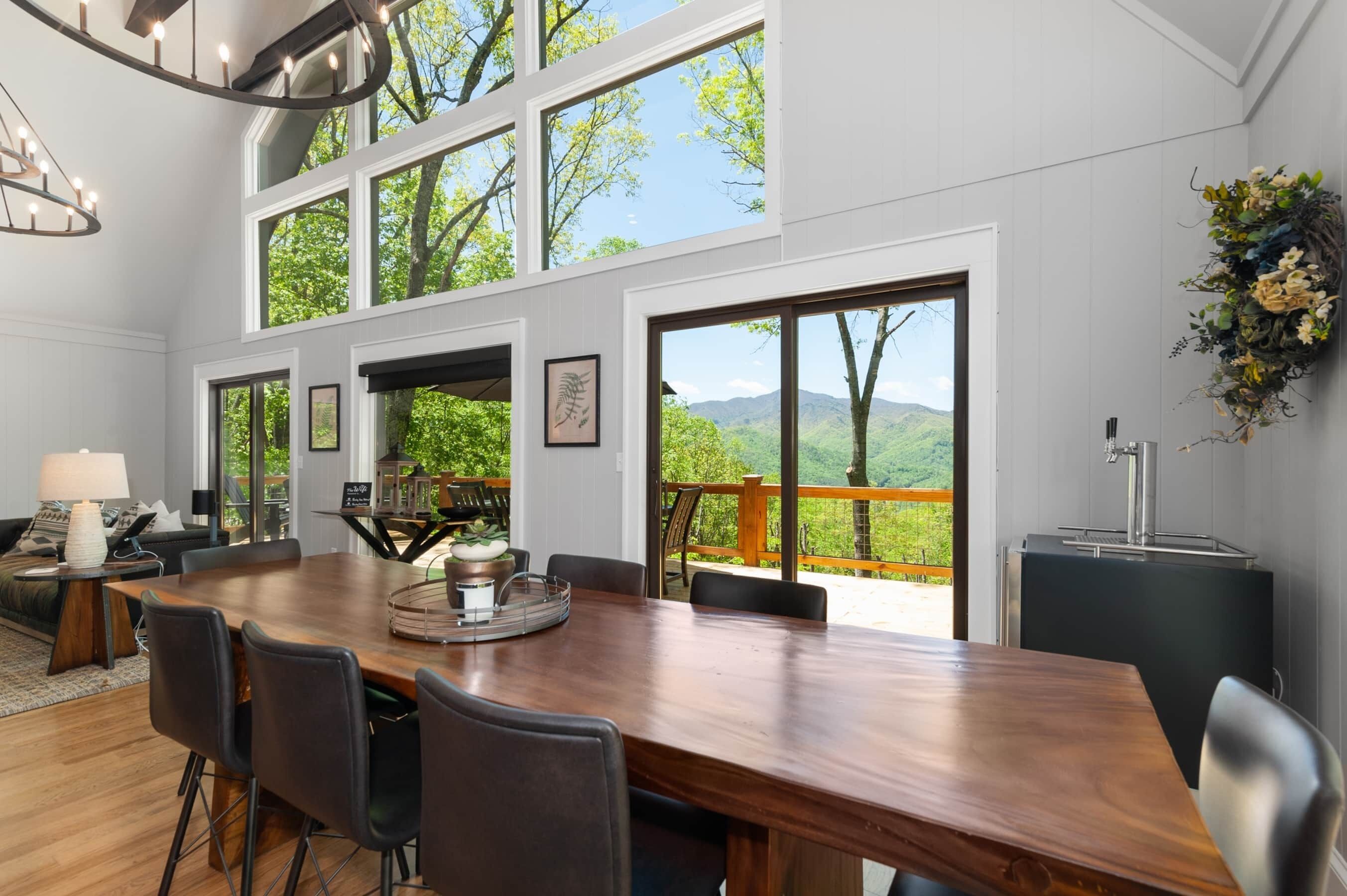 A spacious dining area with a large wooden table, black chairs, and a view of a mountainous landscape through large windows.
