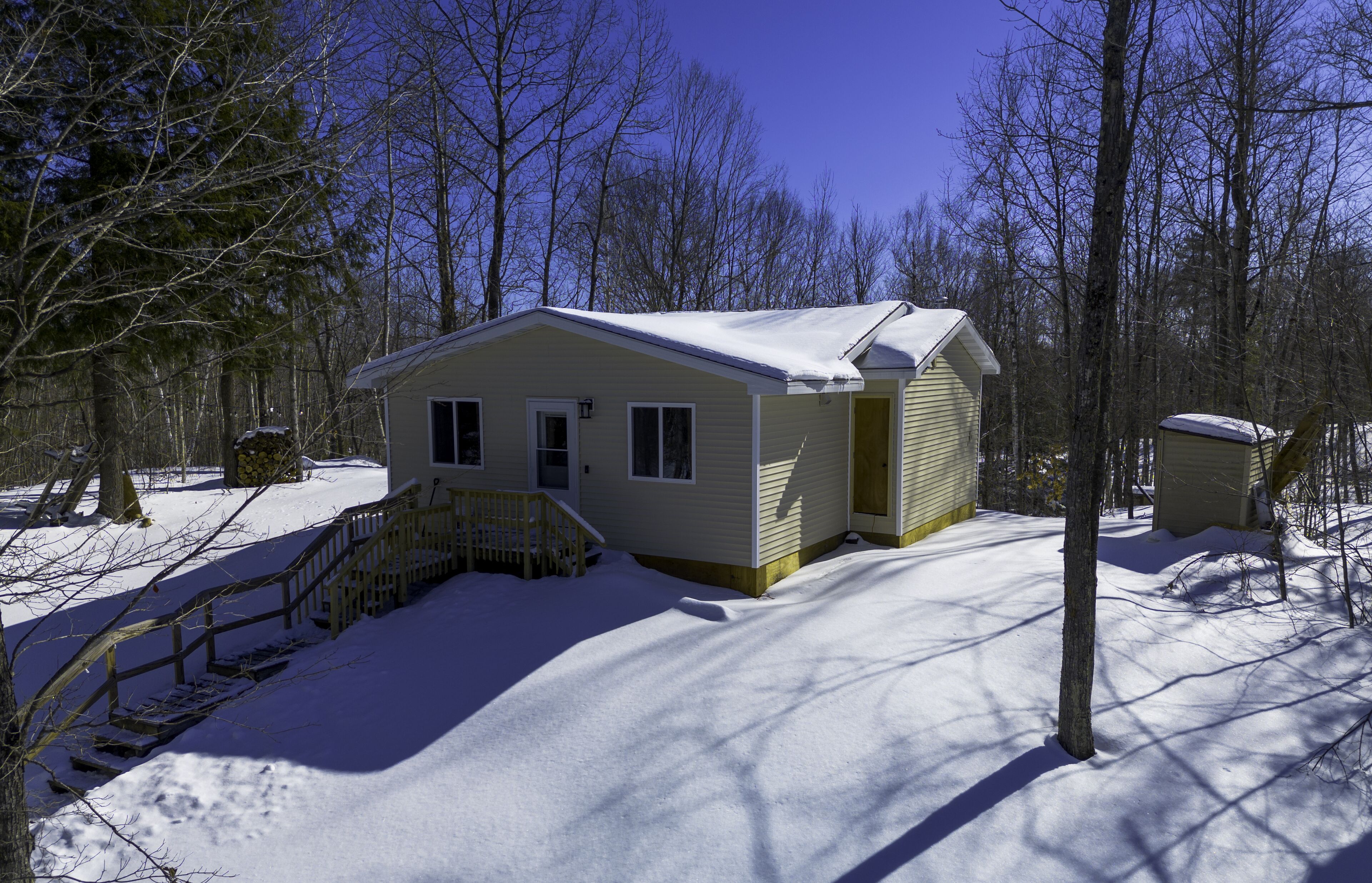 A small, single-story cabin with a covered porch, surrounded by snow and trees.
