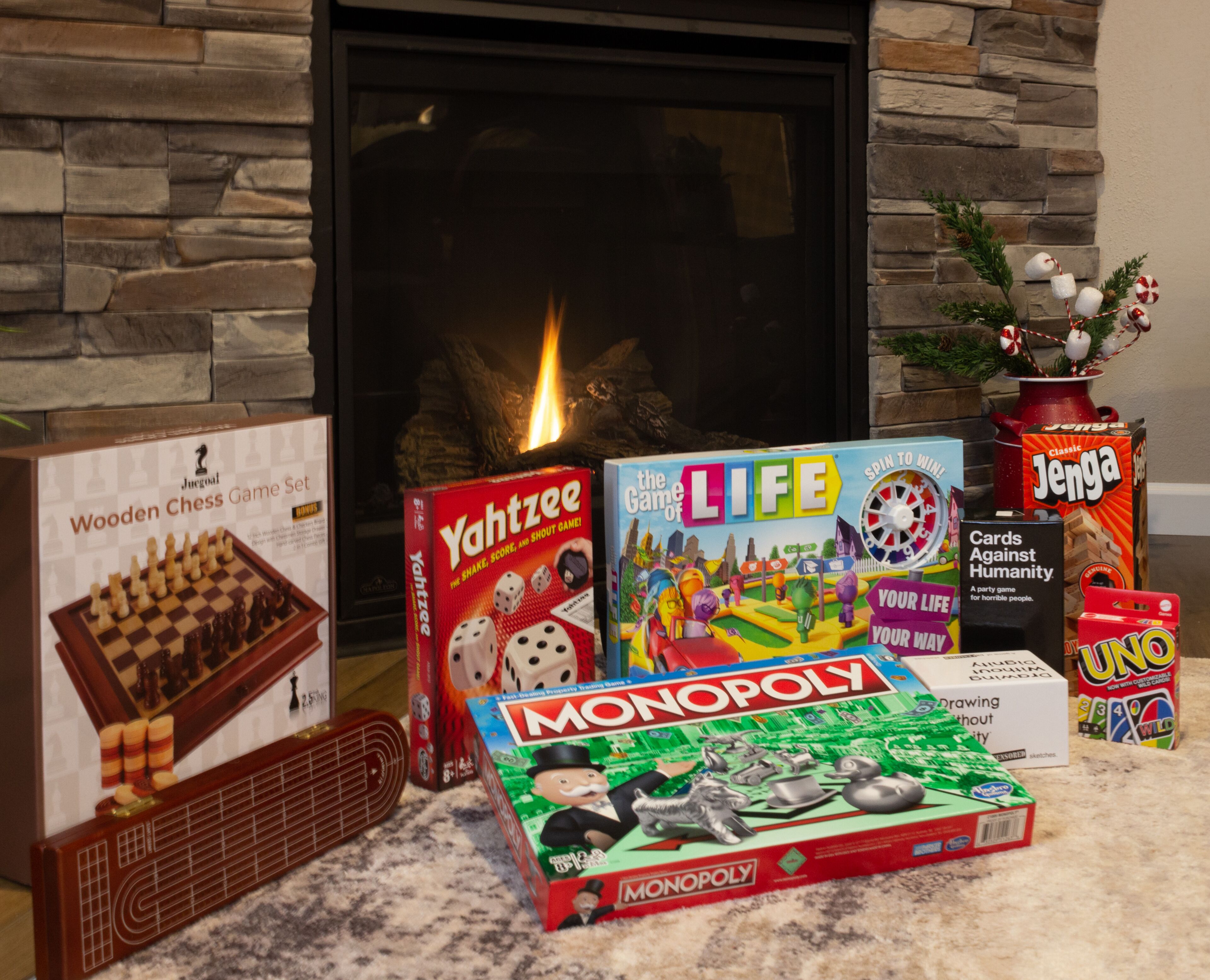 A variety of board games including Monopoly, Yahtzee, and others, arranged on a carpeted floor in front of a fireplace.