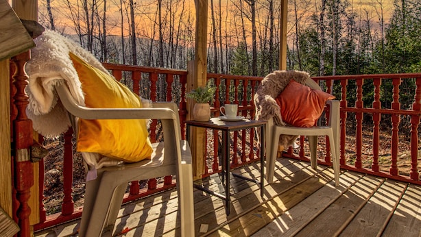 A wooden deck with a red railing, a white chair with a yellow pillow, and a small table with a cup and a plant. - Remodeled Cabin w/fireplace, 2 miles from Lakewood (Mountain)
