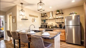 A modern kitchen with a central island, bar stools, stainless steel appliances, and pendant lighting. - Remodeled Cabin w/fireplace, 2 miles from Lakewood (Mountain)