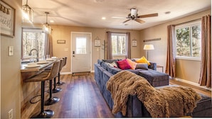 A living room with a sofa, a coffee table, and a dining area with a bar stool. - Remodeled Cabin w/fireplace, 2 miles from Lakewood (Mountain)