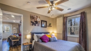 A bedroom with a large bed, a ceiling fan, a window with curtains, and a door leading to another room. - Remodeled Cabin w/fireplace, 2 miles from Lakewood (Mountain)
