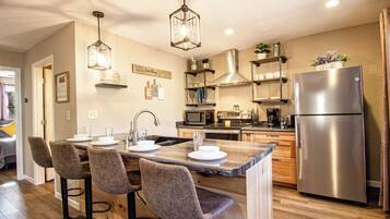 Une cuisine moderne dotée d’un îlot central, de tabourets de bar, d’appareils électroménagers en acier inoxydable et de luminaires suspendus.