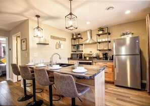 A modern kitchen with a central island, bar stools, stainless steel appliances, and pendant lighting.