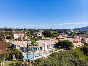 A residential area with houses, a swimming pool, and a hilly landscape in the background.