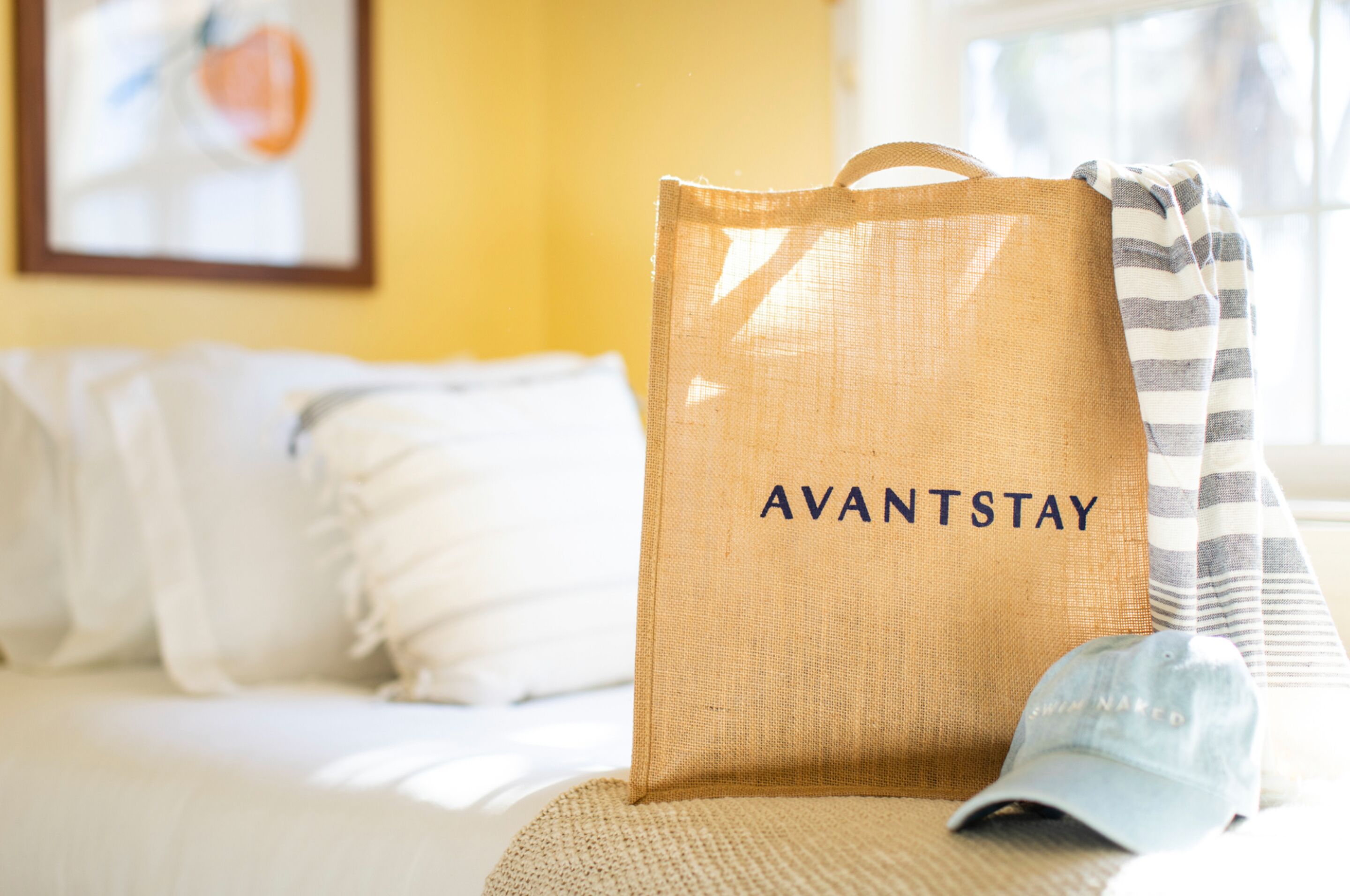Et værelse med en seng, et stribet håndklæde og en jutevæske med teksten "AVANTSTAY".