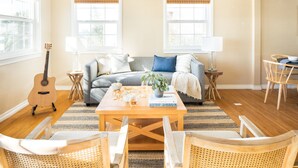 A cozy living room with a sofa, coffee table, and chairs, a guitar, and a dining area with a table and chairs.