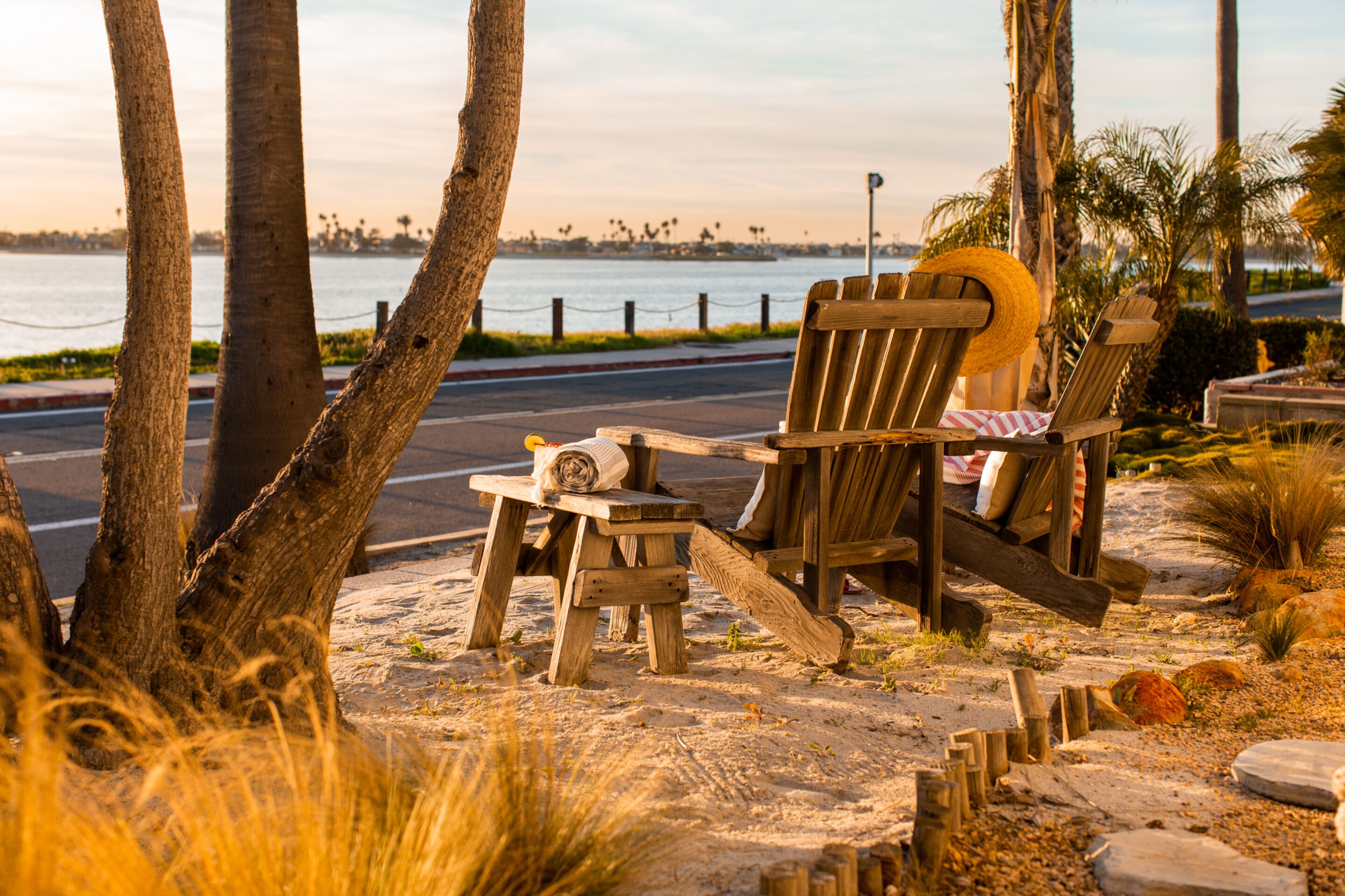 A beachside seating area with wooden chairs and a small table, overlooking a body of water with a distant city skyline.