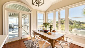 A dining area with a wooden table, white chairs, and a view of the outdoors. - Haven by AvantStay | Luxury Beachfront Home w/ Pool & Gorgeous Patios (Sullivans Island)