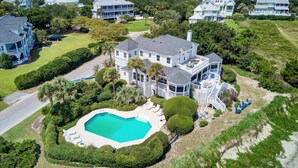 A large, multi-story house with a swimming pool, surrounded by lush greenery and other houses. - Haven by AvantStay | Luxury Beachfront Home w/ Pool & Gorgeous Patios (Sullivans Island)