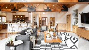 Een ruime woonkamer met een bank, salontafel en stoelen. Achtergrond is een keuken met een bar.
