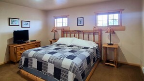 A bedroom with a wooden bed, two bedside tables, a television, and two windows with wooden frames.