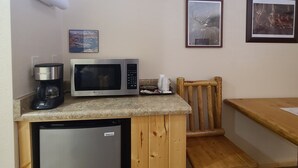 A compact kitchen with a refrigerator, microwave, coffee maker, and a wooden table.