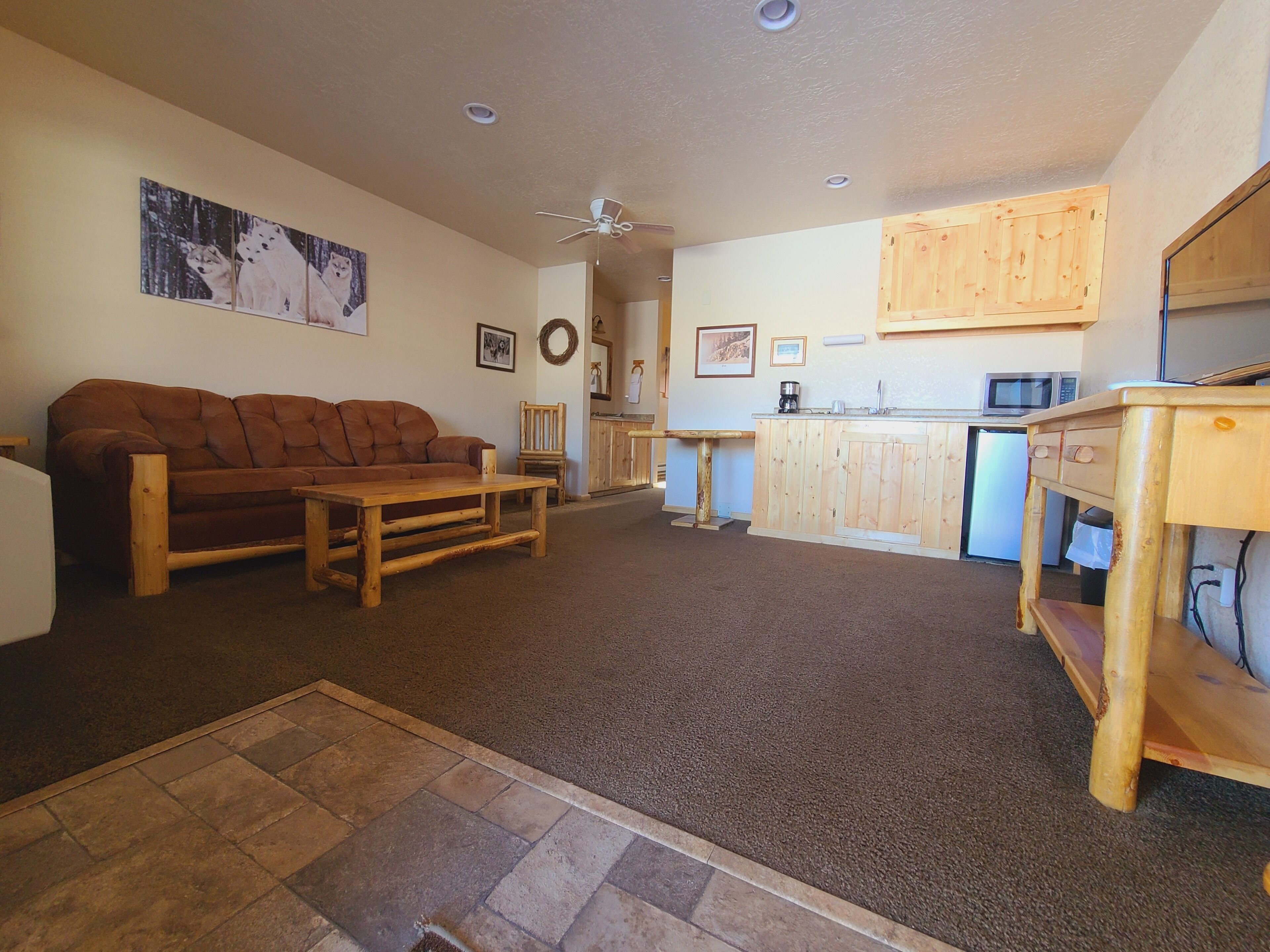 A cozy living room with a brown sofa, wooden coffee table, and a kitchen area with wooden cabinets and a microwave.