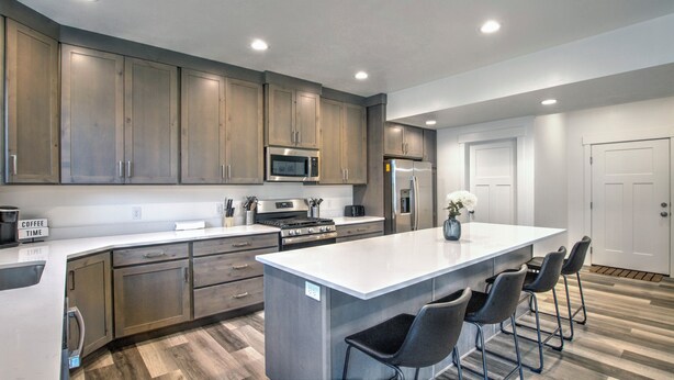 A modern kitchen with wooden cabinets, stainless steel appliances, and a central island with bar stools. - Boat Harbor House - Pool & Hot Tub Access in Unbeatable Location! (Garden City)