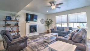 A living room with a fireplace, a ceiling fan, and a large window. - Boat Harbor House - Pool & Hot Tub Access in Unbeatable Location! (Garden City)