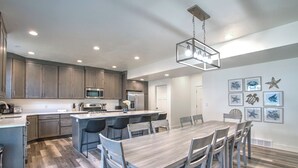 A modern kitchen with a central island, built-in appliances, and a dining area with a large wooden table and chairs. - Boat Harbor House - Pool & Hot Tub Access in Unbeatable Location! (Garden City)