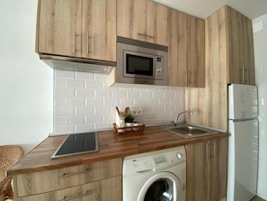 A compact kitchen with wooden cabinets, a built-in microwave, a washing machine, and a refrigerator. - Benal Beach (Benalmádena)