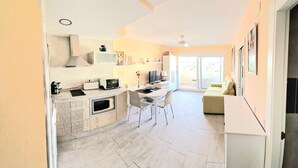 A modern kitchen with white cabinetry, a dining area with a white table and chairs, and a living area with a sofa and a TV. - Benal Beach (Benalmádena)