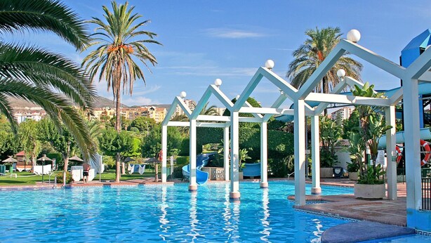 A swimming pool with a clear blue water surface, surrounded by palm trees and a white gazebo structure. - Benal Beach (Benalmádena)