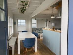 Eine geräumige Küche mit Holzarbeitsplatte, ein Essbereich mit weißem Tisch und blauen Stühlen sowie Meerblick durch große Fenster.