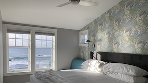 Une chambre à coucher avec un lit, une fenêtre donnant sur l’océan, un ventilateur de plafond et un papier peint à motifs.