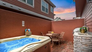 A hot tub in a backyard with a brick patio, a table with chairs, and a stone wall with a sink. - Comfy Villa | 5 Min to Dinsey! Hot Tub & BBQ* (Kissimmee)