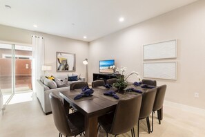 A modern dining area with a table set for six, a sofa, a TV, and artwork on the walls.