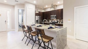 A modern kitchen with a central island, bar stools, stainless steel appliances, and pendant lighting. - Comfy Villa | 5 Min to Dinsey! Hot Tub & BBQ* (Kissimmee)
