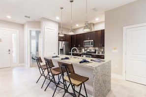 A modern kitchen with a central island, bar stools, stainless steel appliances, and pendant lighting.