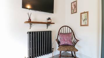 A room with a radiator, a chair with a floral cushion, a shelf with decorative items, and a mounted television.