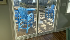 A room with a sliding glass door leading to an outdoor deck with blue Adirondack chairs and a table. - Completely Renovated in 2022! Perfect Location! (Kill Devil Hills)