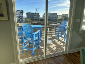 A room with a sliding glass door leading to an outdoor deck with blue Adirondack chairs and a table.