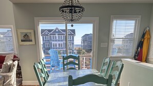 A dining area with a wooden table and matching chairs, a chandelier, and a view of houses through large windows. - Completely Renovated in 2022! Perfect Location! (Kill Devil Hills)