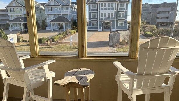 A wooden deck with two white Adirondack chairs and a small table, overlooking a row of houses. - Completely Renovated in 2022! Perfect Location! (Kill Devil Hills)