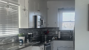 A modern kitchen with white cabinets, a granite countertop, a stainless steel refrigerator, and a microwave. - Completely Renovated in 2022! Perfect Location! (Kill Devil Hills)