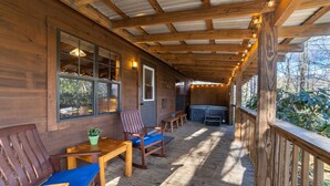A wooden deck with a covered area, wooden chairs, a table, and a potted plant. - Wooded Couples Log Cabin w/ Hot Tub (Pet-friendly) (Hot Springs)