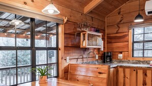 A wooden cabin interior with a kitchen area, a dining bench, and a window with a view of trees. - Wooded Couples Log Cabin w/ Hot Tub (Pet-friendly) (Hot Springs)