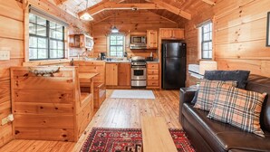 A cozy cabin interior with wooden walls, a kitchen with modern appliances, a dining area, and a living room with a couch and pillows. - Pet-Friendly Mountain Log Cabin for Couples (Hot Springs)