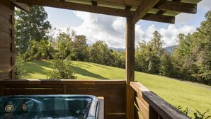 A hot tub in a wooden deck with a view of a grassy landscape and trees. - Pet-Friendly Mountain Log Cabin for Couples (Hot Springs)
