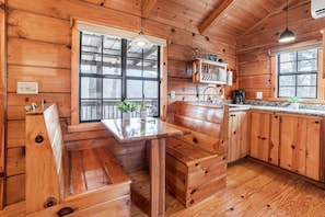 A wooden cabin interior with a kitchen area, wooden bench seating, and a window providing natural light. - Honeymoon Log Cabin w/ Wooded Mountain Views (Hot Springs)