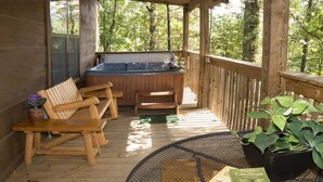 A wooden deck with a hot tub, wooden chairs, a round table with a book, and a potted plant.