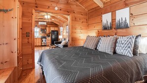 A wooden cabin interior with a bed, a kitchen area, and a dining table.