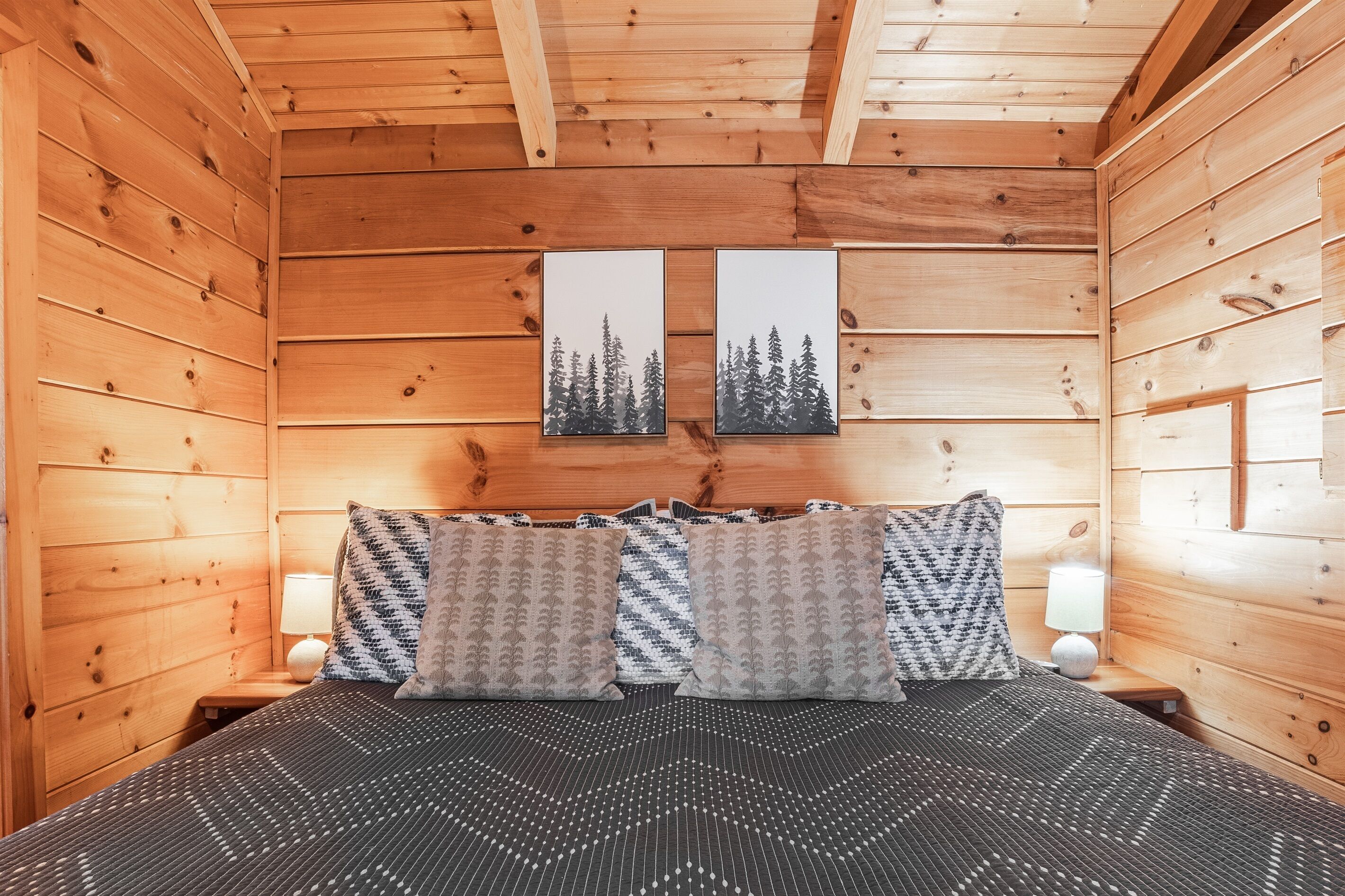 A wooden cabin room with a bed, two nightstands, and two wall-mounted picture frames.